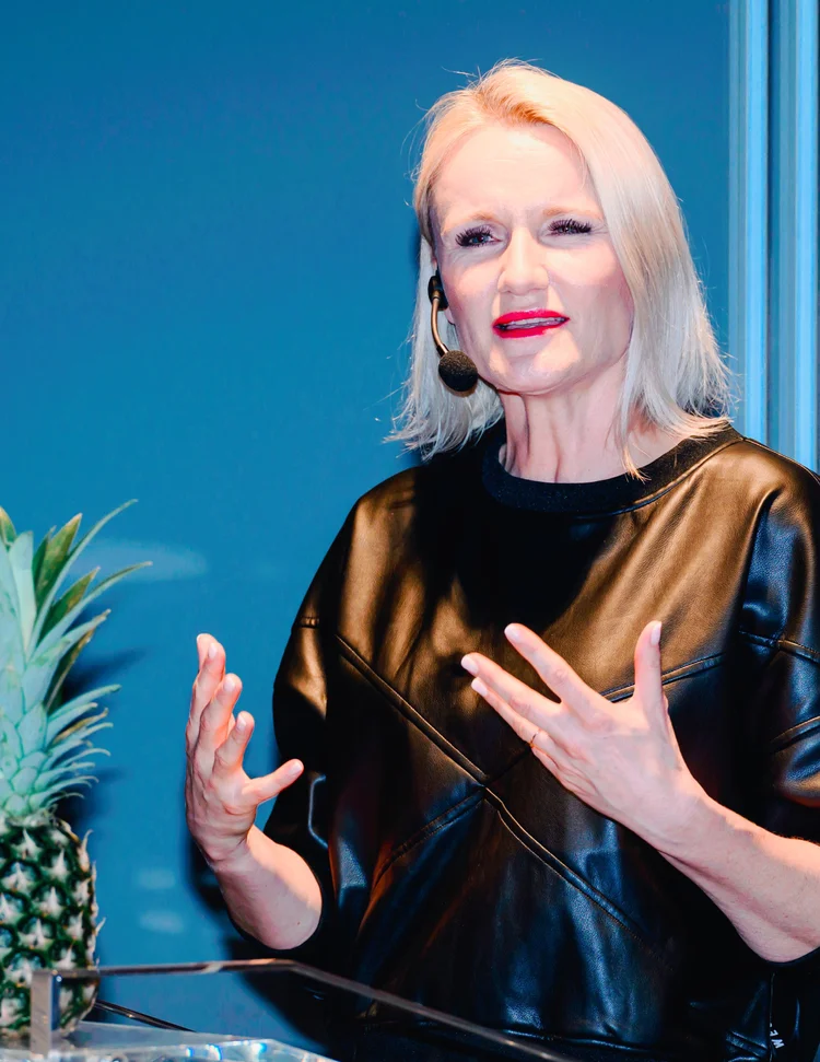 Henriette Hochstein-Frädrich Keynote-Speakerin mit Ananas und Lederoberteil vor blauer Bühne – Vortrag zu Innovation und Wandel