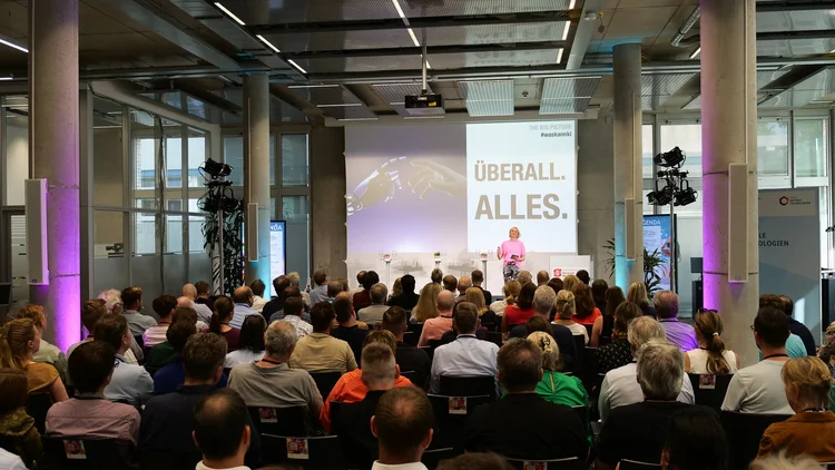 Henriette Frädrich als Keynote-Speakerin auf der Bühne vor dem Slide „Überall. Alles." · Sammelbeitrag Juni 2024