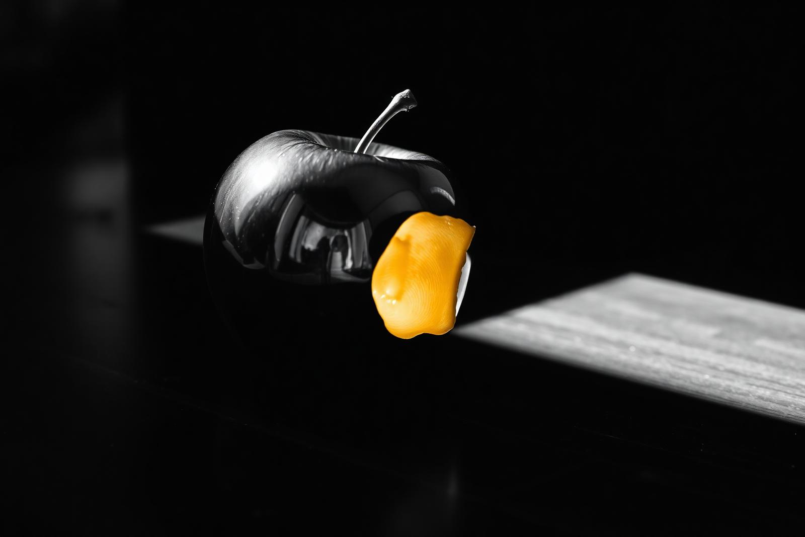 Cinematisches Schwarz-Weiß-Editorial-Stillleben auf dunklem Holz: ein chromglänzender Apfel mit einer einzelnen warm-goldenen Bissstelle als einziger Farbfläche im monochromen Bild — Metapher für Perfektionismus als Blockade zwischen Anspruch und Fortschritt.